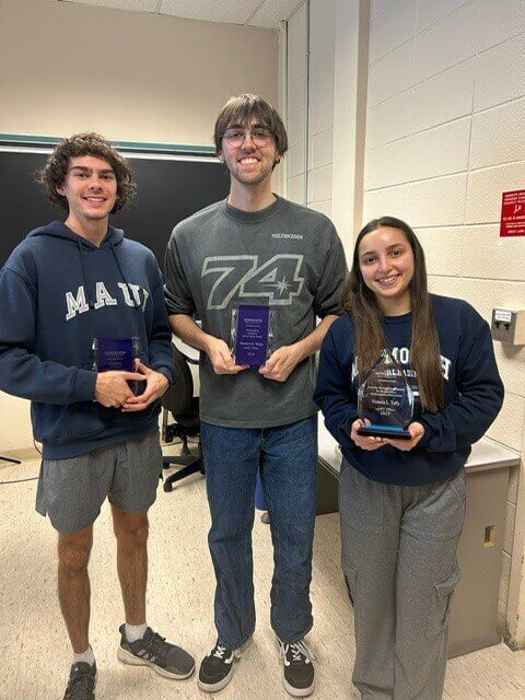 Three students holding statues of their awards