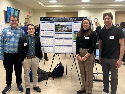 Four students stand in front of poster presentation