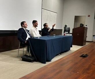 Panelists at table, with one professor holding mic and speaking