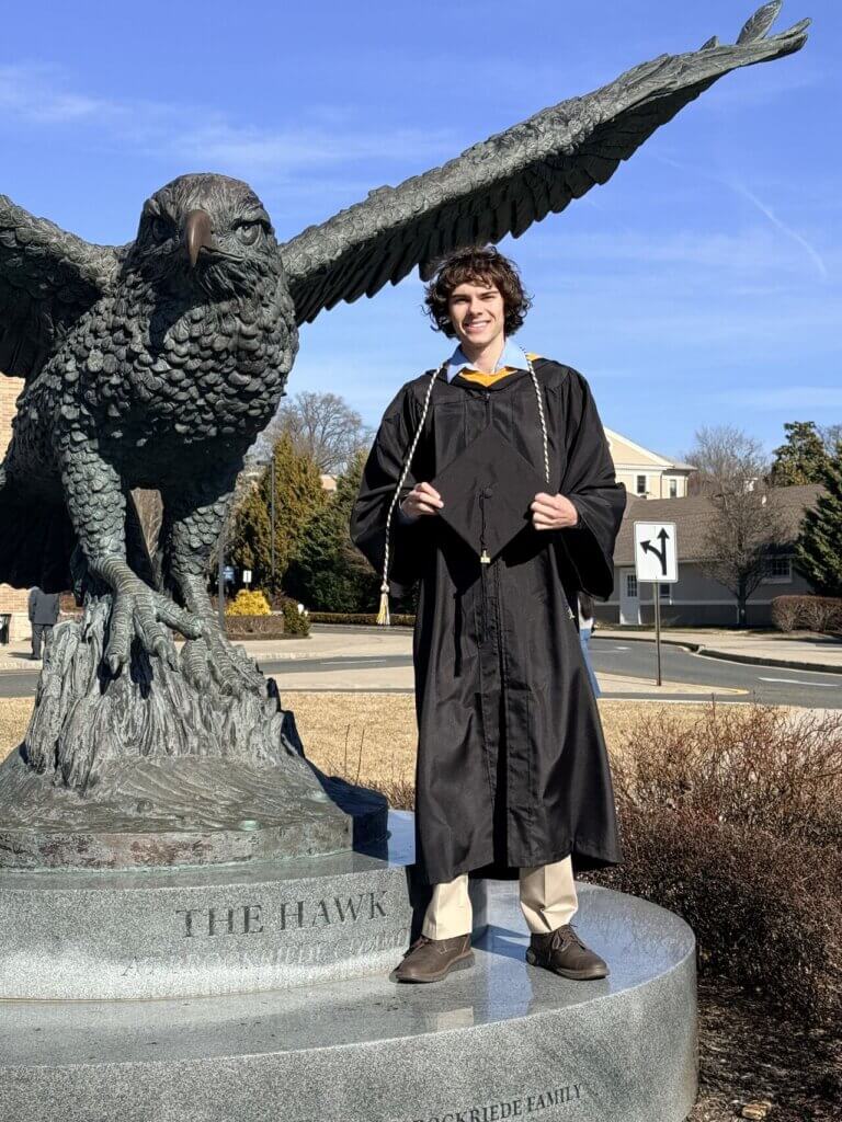 Graduate in Cap and Gown standing near large hawk statue
