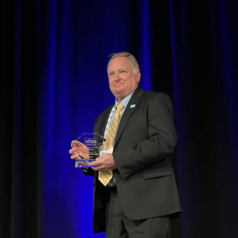 Man in suit holding award in front of blue curtains
