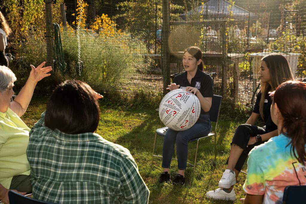 A women is giving a lecture to a small group in front of a garden