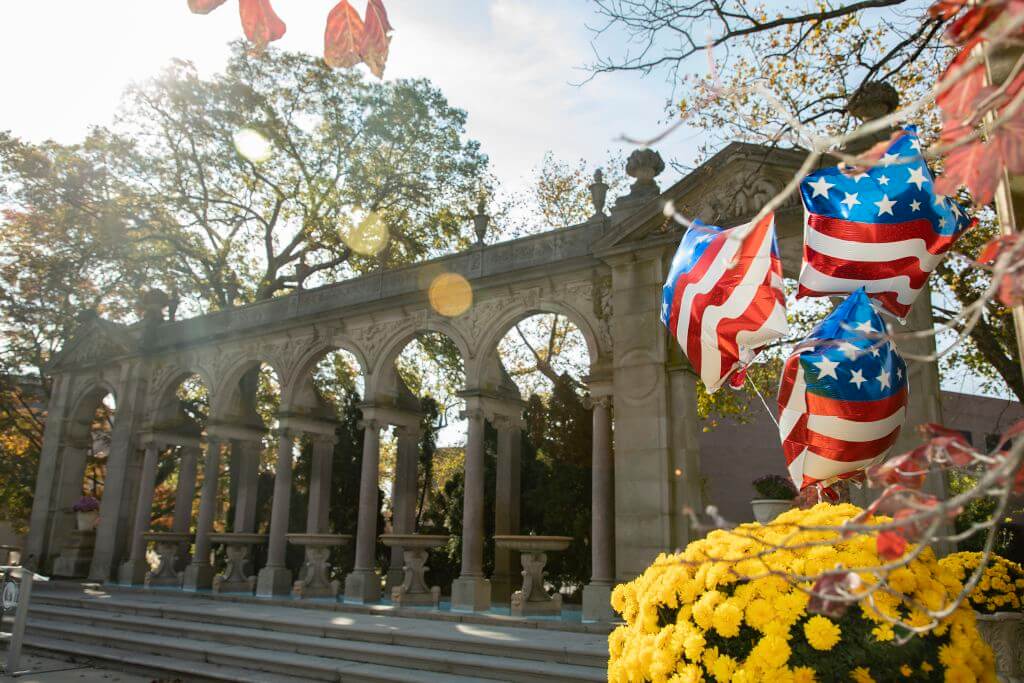 A stone archway with fountains is in the background with star shaped balloons that have an American flag motif on them. 