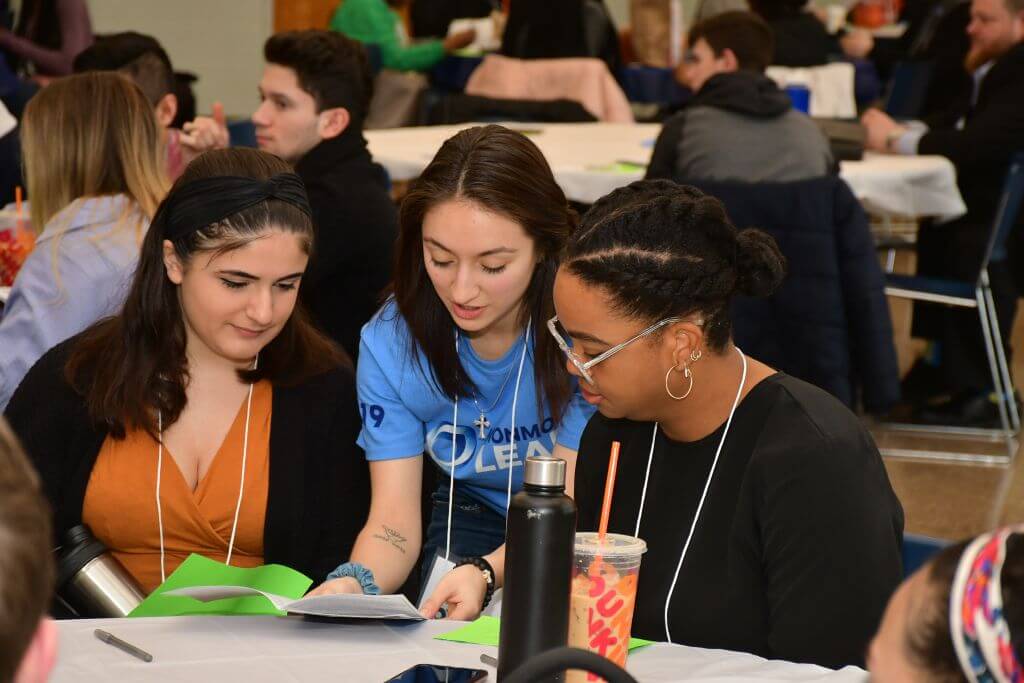 At the Monmouth LEADS conference, a student leader reviews the program guide of the event with 2 student attendees.