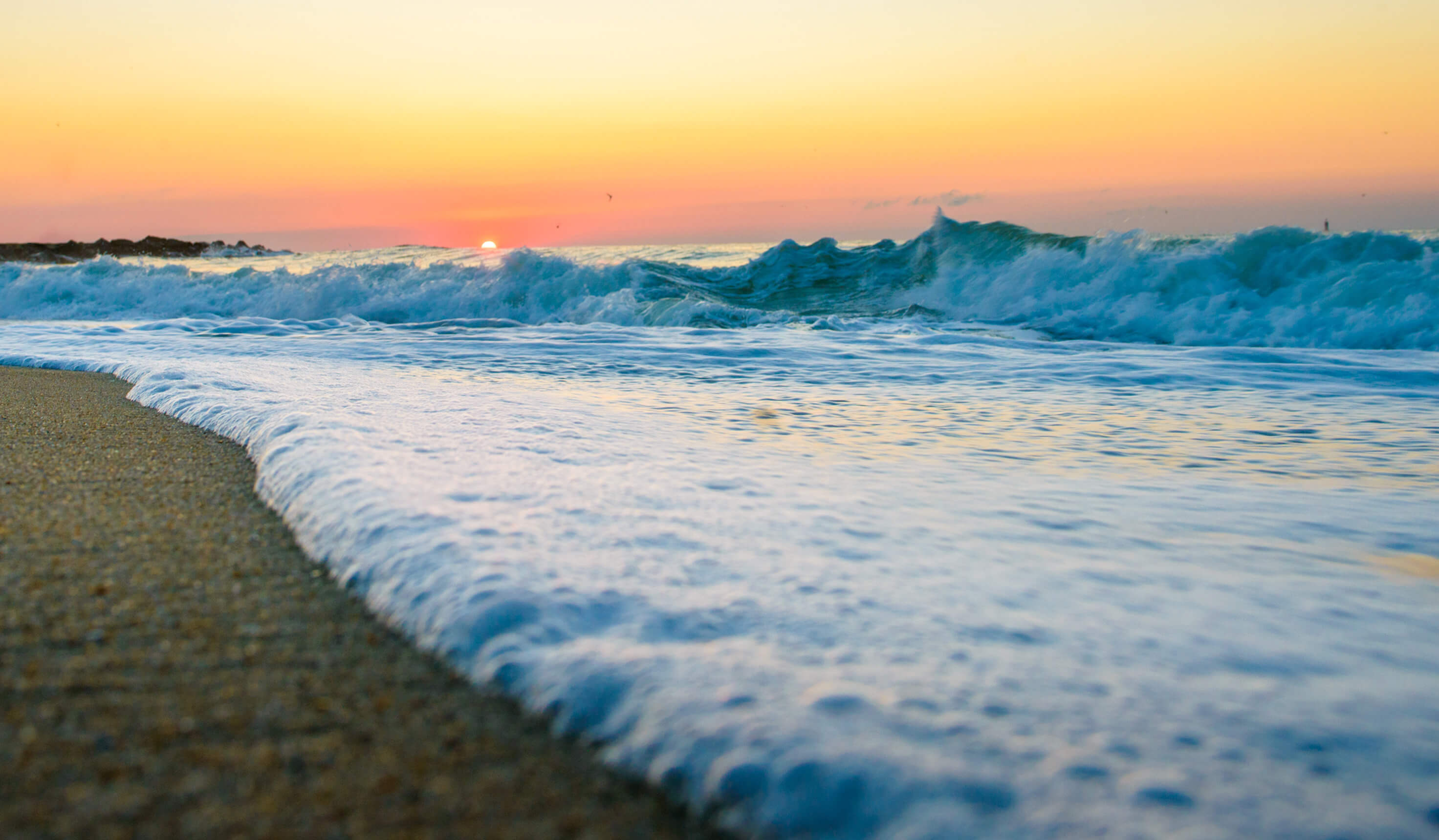 Picture of a small wave washing on the beach, sunrise in the background.