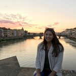 A student sitting on a stone bridge over a river in Florence.