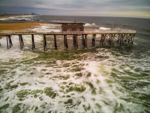 Photo shows storm waves breaking against pier at the beach