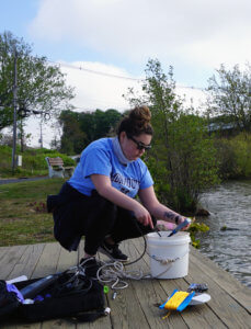 A student is bending over a bucket with a device to take a sample of water from it.