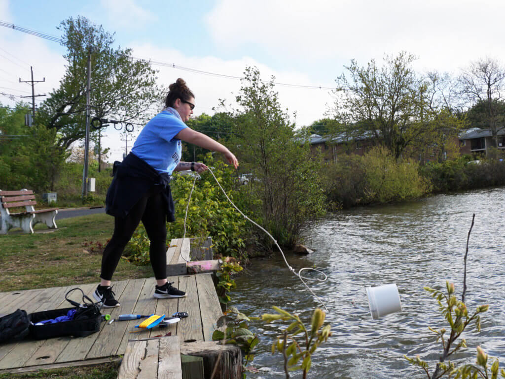 A woman throwing a sample bucked into a body of water