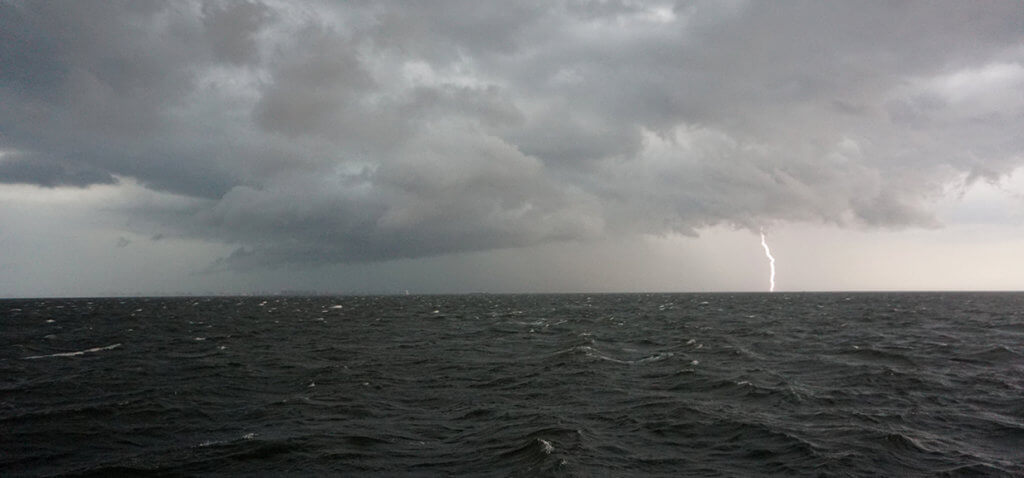 Photo shows storm clouds and lightening bolt on the horizon