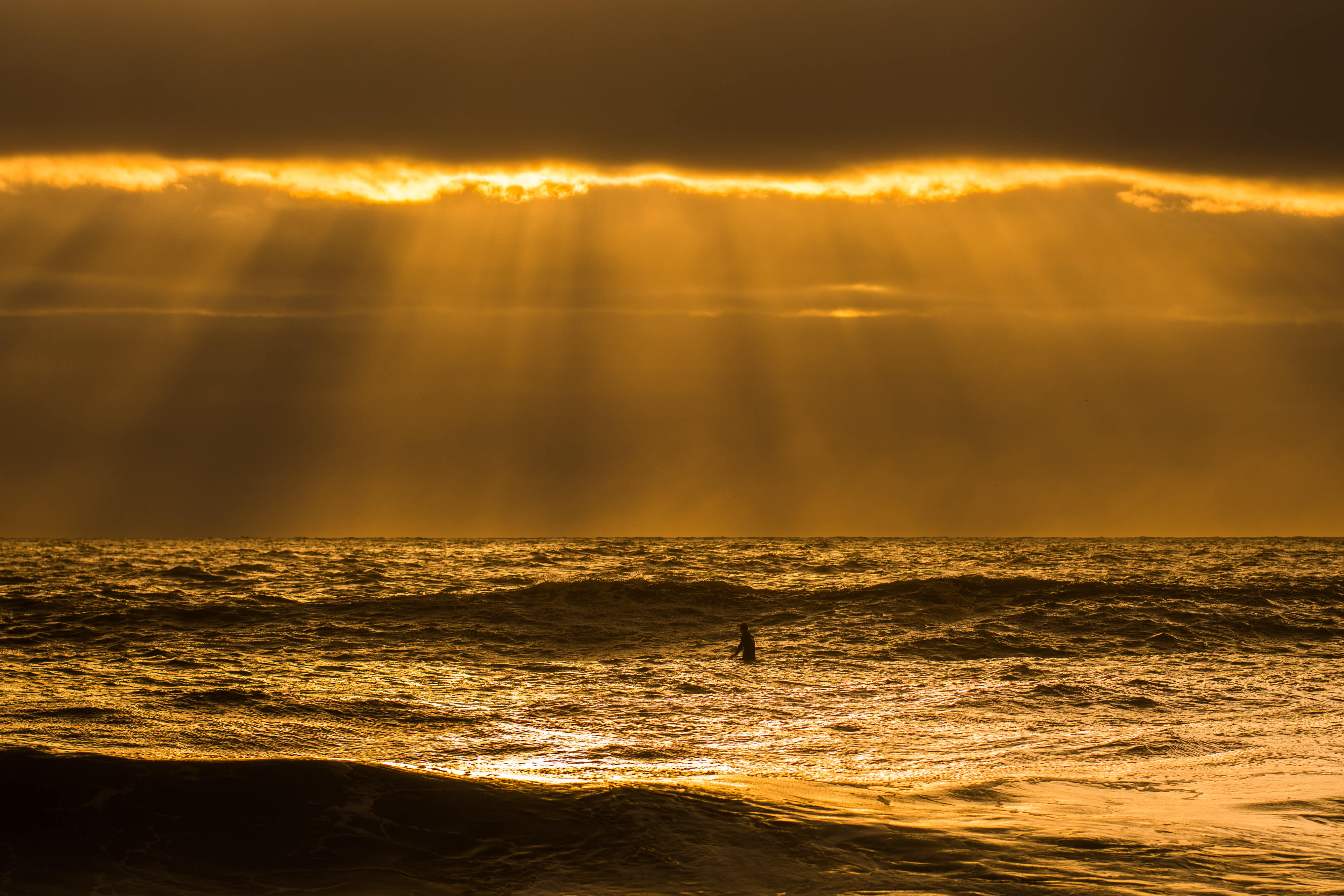 Dramatic sunset photo at the beach with lone swimmer in ocean