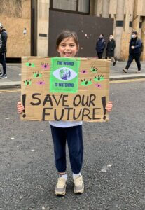 Photo of young child holding sign at COP26 which states "Save Our Future"