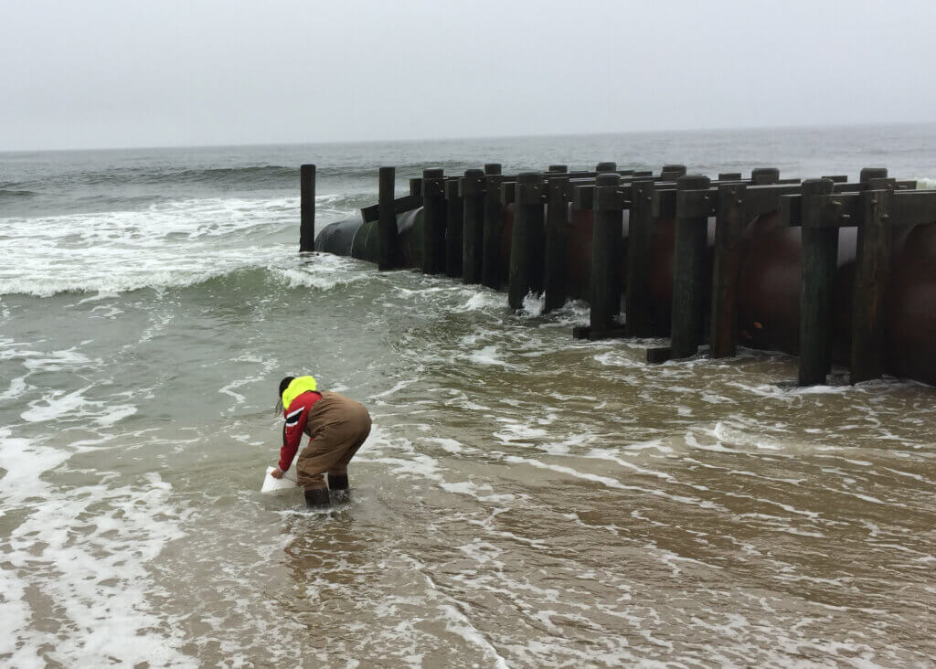 A student gathers a water sample near a drainage pipe in Long Branch.