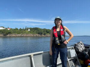 Mauro standing aboard a vessel with a rocky shoreline in the background. 