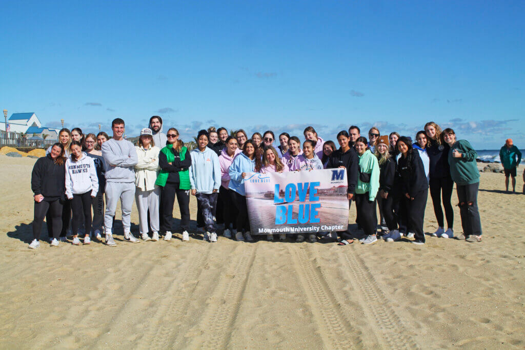 Students posing with a Love Blue banner on the beach.