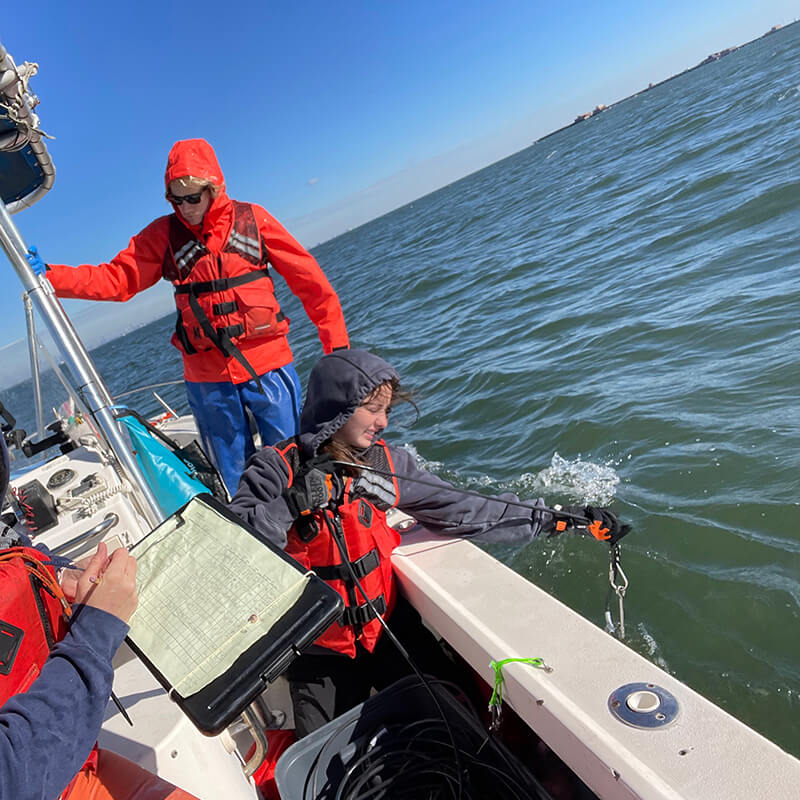 A woman leaning over the side of a vessel pulling a rope out of the water