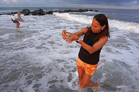Volunteers from the Surfrider Foundation stand along the waterline, gathering ocean water samples.