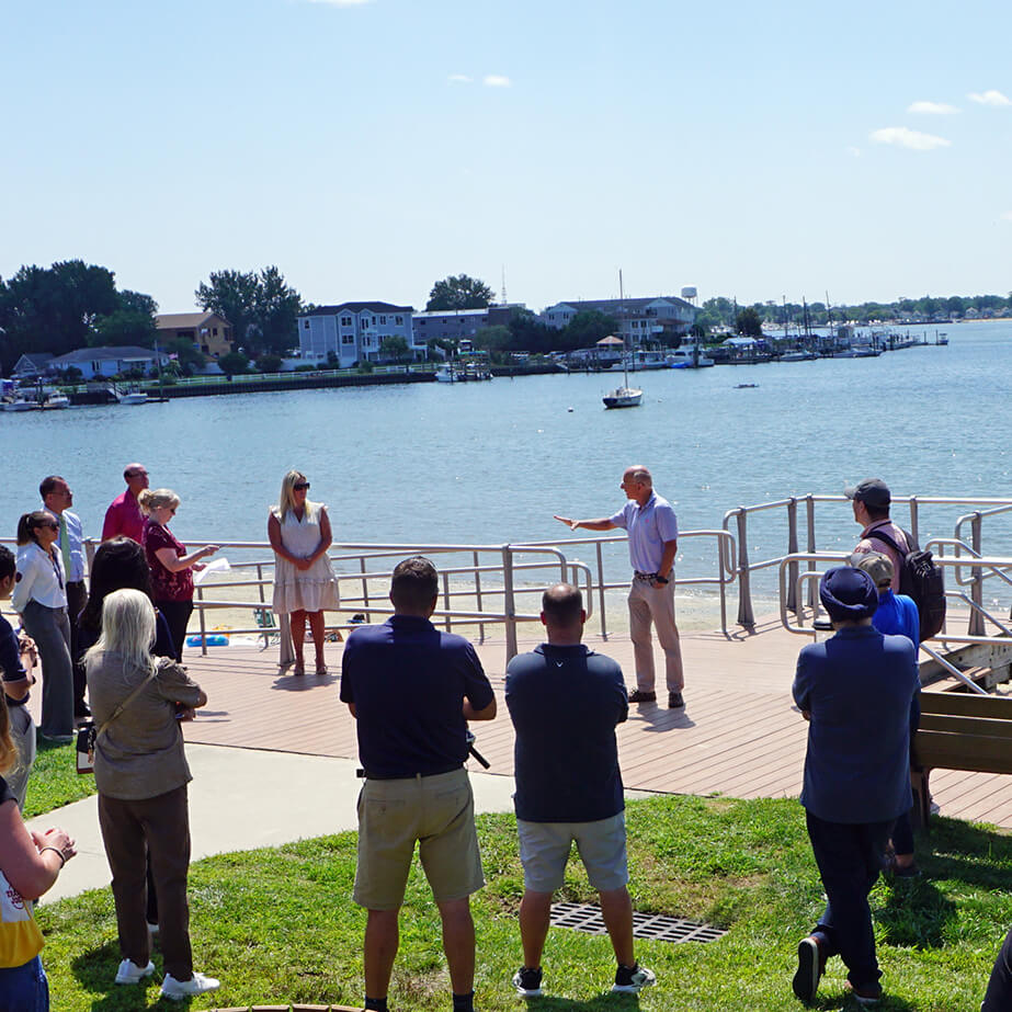 People gather around a speaker at a bayfront beach.