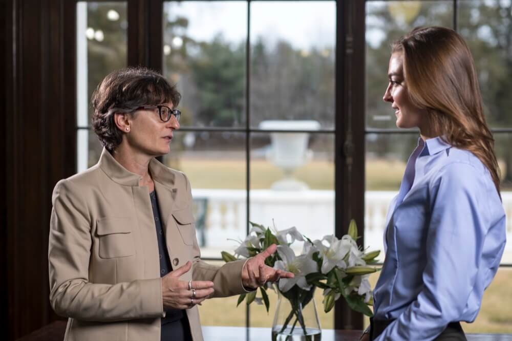 Two women talking in front of a window