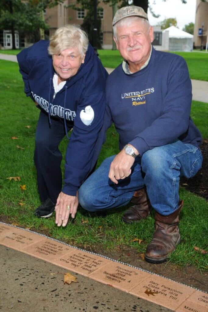 Two people kneeling by the hawk walk, one in Monmouth University regalia and the other with a United States Navy shirt