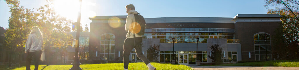 A student walking past a building with the sun shining in the background.